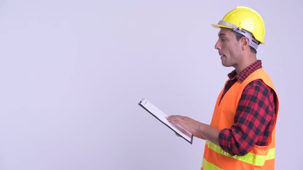 Profile View of Young Happy Hispanic Man Construction Worker Showing Clipboard and Giving Thumbs Up