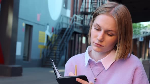 Thoughtful Blonde with Short Hair Looks Around and Writes alt