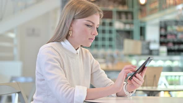 Young Woman Celebrating Success on Smartphone in Cafe  alt