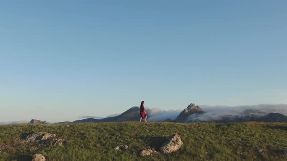 Young Sexy Woman in a Red Dress Walks Along the Top of the Hill in the Rays of the Sunset Against alt