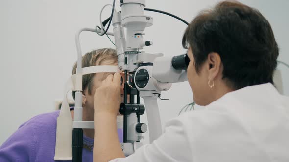 Female Doctor Is Using Optic Tool To Check Patient's Vision. Patient in Eye Clinic. alt