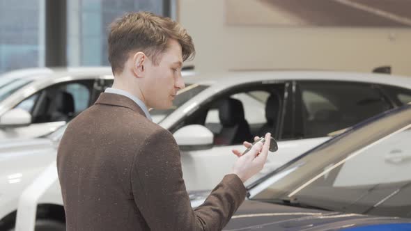 Cheerful Mature Man Smiling to the Camera Holding Car Keys at the Dealership alt