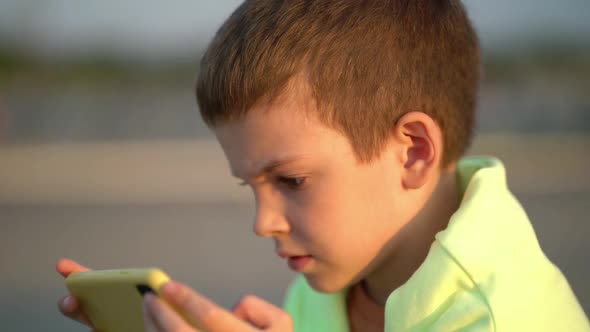 Boy Watching Cartoons on His Phone While Sitting on a Bench in the Park