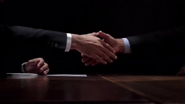 Anonymous business partners making handshake after confidential meeting in dark room