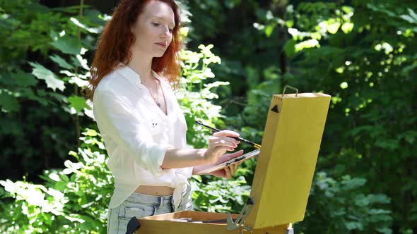 Young Red-Haired Woman With an Easel in The Forest