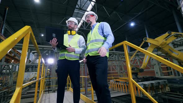 Colleagues Stand in a Factory Facility, Checking the Work of Factory Machines. alt