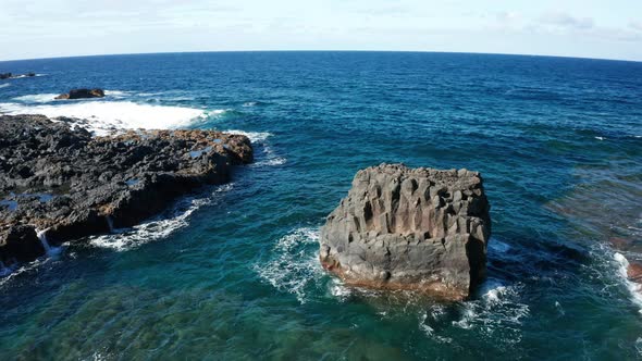 Aerial arc shot around small island of basalt columns in ocean surf alt
