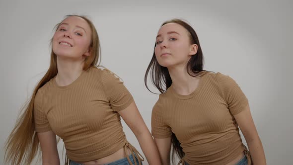 Slim Beautiful Identical Twin Sisters Dancing Simultaneously at Grey Background Looking at Camera alt