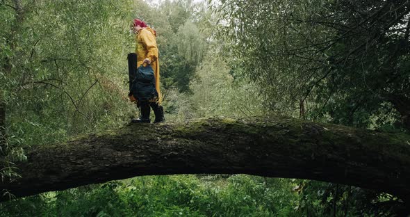 Hiker in a Yellow Raincoat with Backpack Walking on a Fallen Tree in the Forest