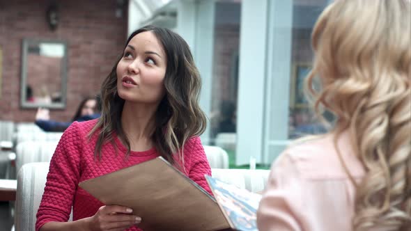 Young Woman with a Friend Ordering To Waiter Holding Menu alt