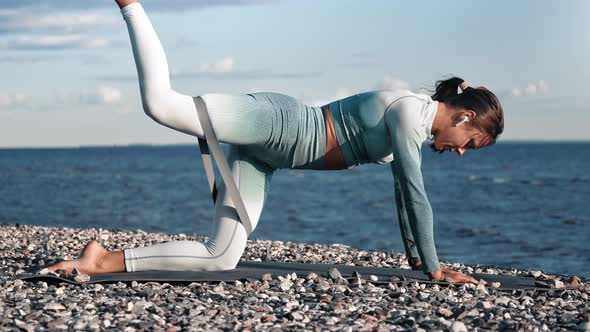 Athletic Woman Lifting Leg Training Buttocks with Exercise Rubber at Sunset Beach Coast Nature alt