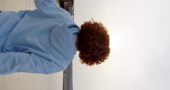 girl with curly hair by the lake doing exercises stretching her arms to her shoulders alt