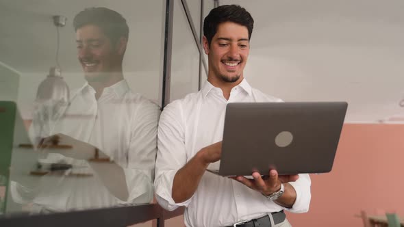 Portrait of Young Latin Guy Standing and Holding Laptop in Contemporary Office Space