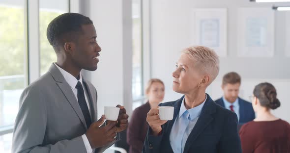 Interracial Business Colleagues Drinking Coffee While Talking in Office alt