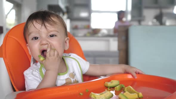 A Smart Kid Eats Avocado Fruits with Pleasure While Sitting at a Feeding Table the Kid Carefully