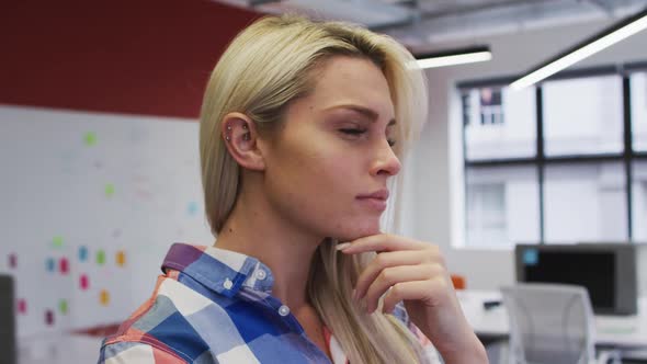 Caucasian businesswoman rubbing her chin in thought and smiling in office alt