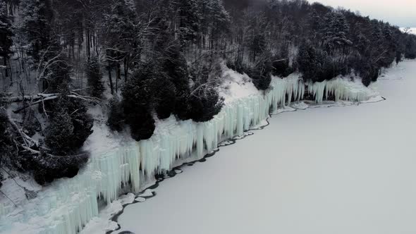 Aerial Flight Over the Cliff Near the Lake From Which Hang Huge Icicles alt
