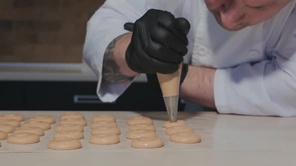 a Caucasian Man Pastry Chef Bent Over the Table and Lays Out Macaroon Dough From a Pastry Bag