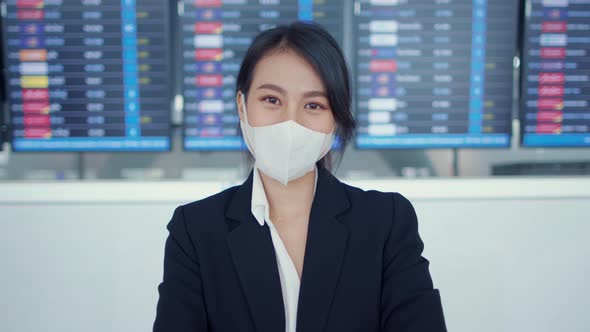 Asian business girl wear face mask stand in front of board flight show time look at camera.