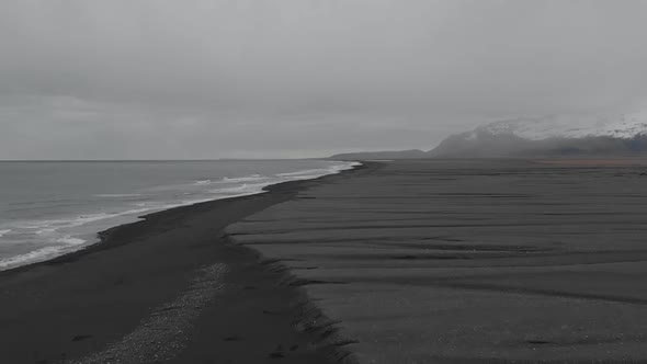Establishing shot flying along the vast landscape of black sand beach. alt