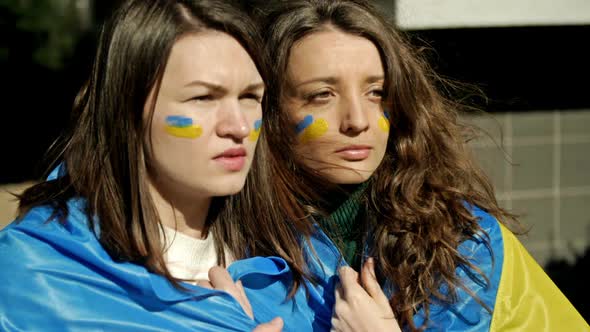 Women with the Flag of Ukraine on Their Shoulders Looking Into the Distance with Excitement and Hope alt