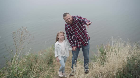 Positive Pretty Girl Looking Away Holding Hands with Smiling Father Pointing alt