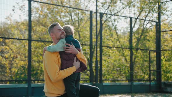 Father Hugs His Son After Basketball Practice and They Go Away on a Sunny Day