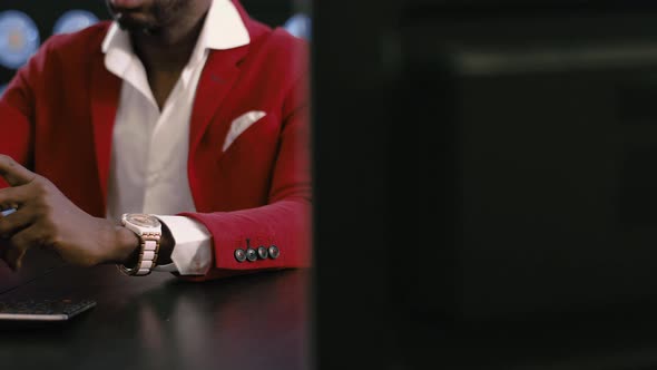 Bearded Africanamerican Businessman in Red Suit Uses Smartphone in Dark Room