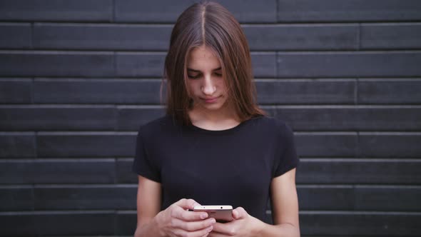 An Attractive Young Lady Wearing Glasses Using a Phone Against a Brick Wall Background. Close-up alt