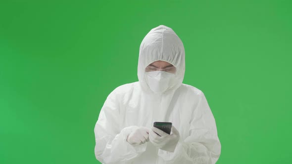 Asian Man Wear Protective Uniform PPE And Use Mobile Phone In The Green Screen Studio alt
