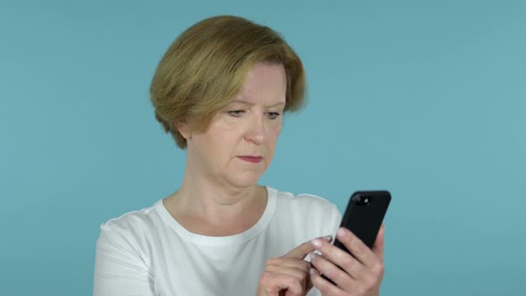 Old Woman Reacting To Loss and Using Smartphone Isolated on Blue Background alt