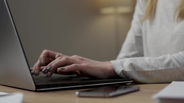 Close up view of the young caucasian woman sitting at the desk with laptop, typing an email alt