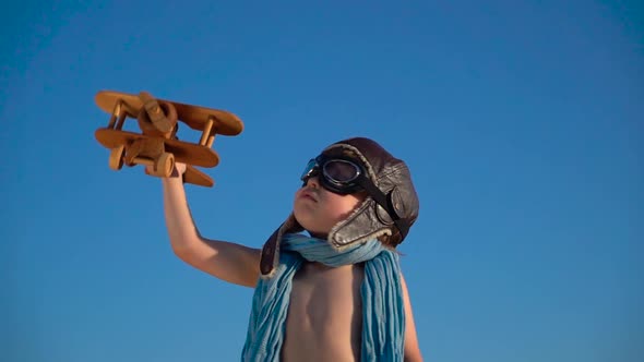 Happy child playing with vintage wooden airplane against blue sky background.