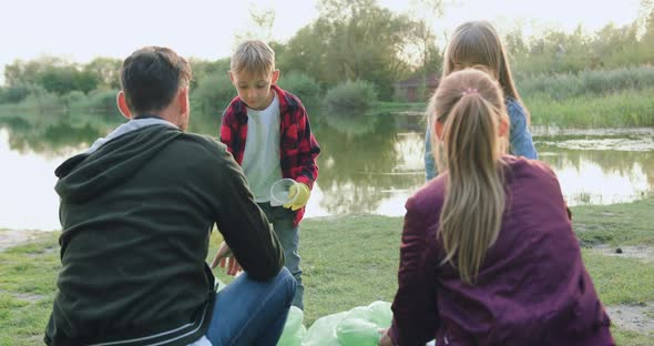 Boy and Girl Helping their Parents to Collect Rubbish from Lake's Shore and Giving High Five alt