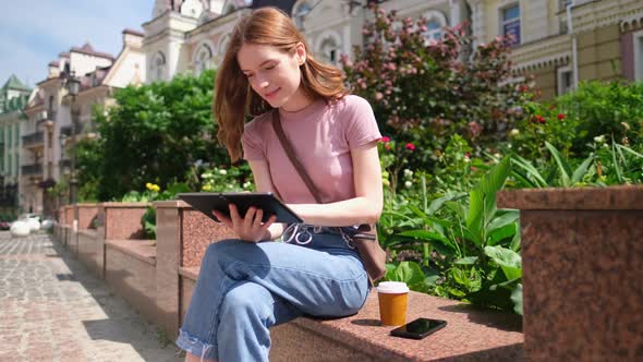 Beautiful Young Woman Tourist with Takeout Coffee in the City Center Using Tablet Pc alt