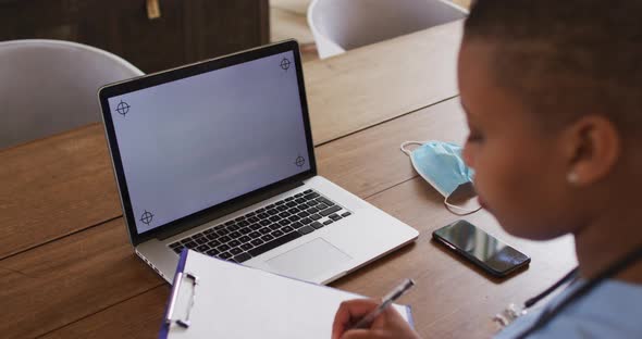 African american female doctor making notes during video call using laptop with copy space alt