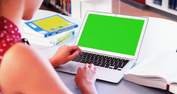 School girl using laptop in library alt