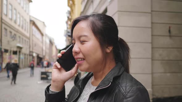 Happy Asian woman standing and having a call on street in Sweden alt