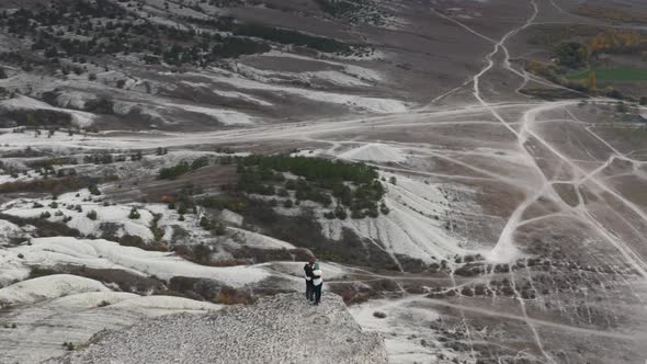 Aerial Panoramic View Active Hiker Couple Hugging on Top of White Rock Surrounded By Hilly Terrain alt