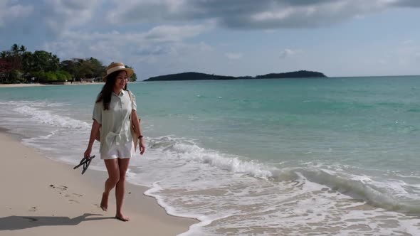 Slow motion of a beautiful young asian woman with hat and bag strolling on the beach