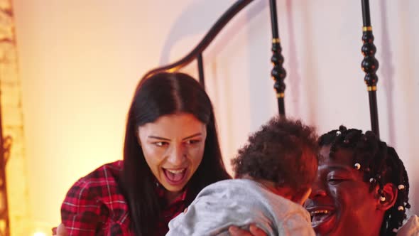 AfricanAmerican Father Tossing His Curlyhaired Toddler Up and Down on Bed alt