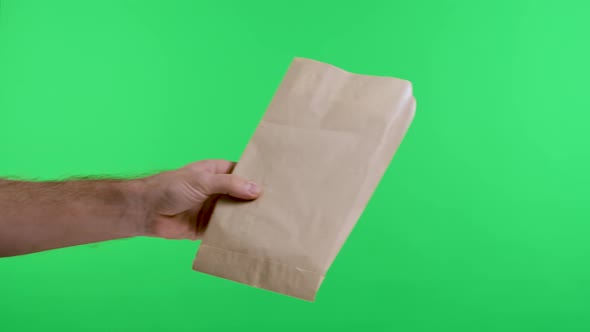 A Man's Hand Gives a Paper Shopping Bag to a Woman's Hand Against the Background of a Green Screen alt