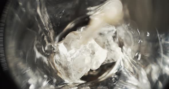 Putting ice cubes and pouring alcohol liquor beverage in a glass - close-up cinematic top-view