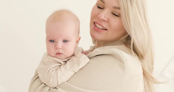 Portrait of a Young Mother Blonde Holding a Newborn Baby in Her Arms Indoors