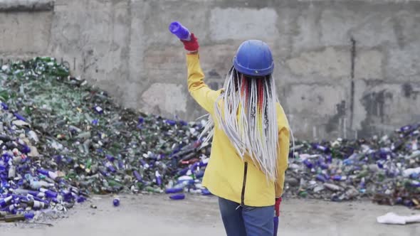 Woman in Hard Hat Standing Against the Pile of Broken Glass Used Bottles Next to the Wall alt