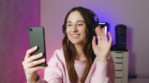 Young Smiling Woman in Headphones Talking to Boyfriend in Video Chat Using Smartphone alt