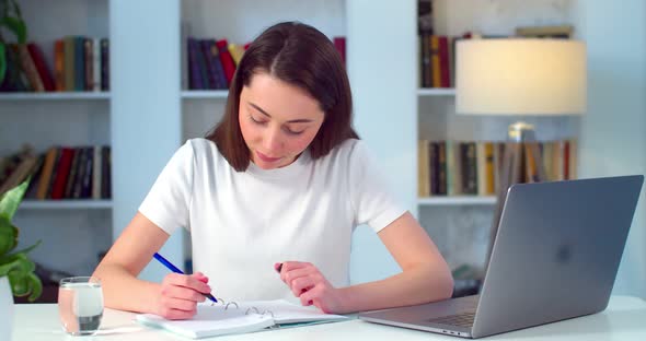 Young Woman Taking Notes While Working on Laptop Indoors Apartment Background
