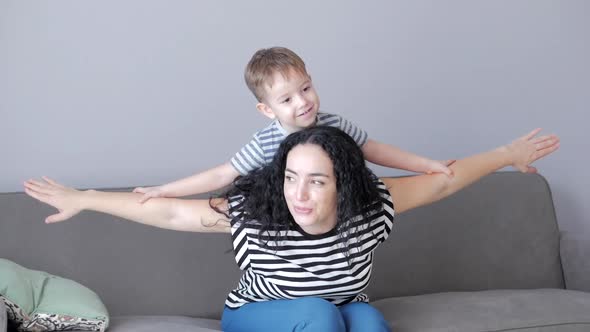 Happy Healthy Family Young Mom Lifting Cute Little Child Son Up Playing Plane on Sofa at Home, Funny alt