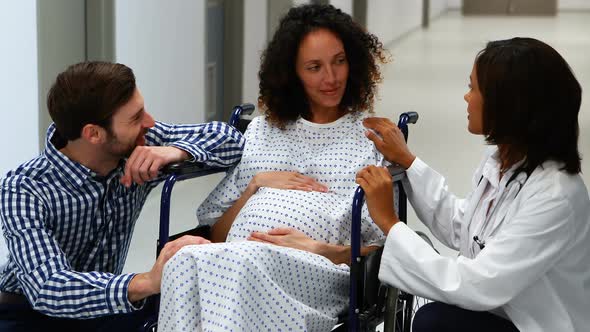 Doctor and man interacting with pregnant woman in corridor alt