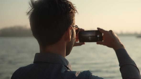 Man Holding Mobile Phone And Taking Picture At Sunset.Close Up Attractive Man Happy Using Mobile App alt
